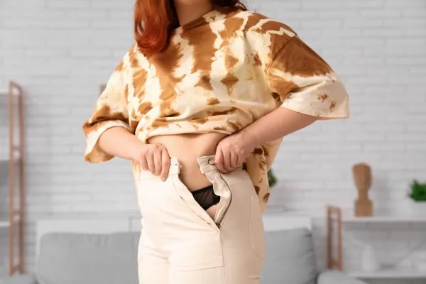 Image of woman trying to do her trousers up after pregnancy weight gain Barr Common