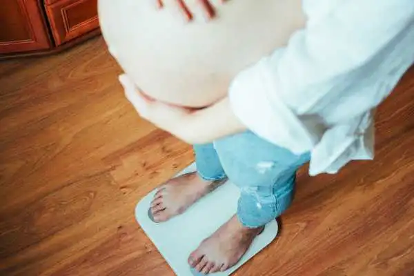 Image of woman weighing herself and experiencing weight gain through pregnancy Barr Common
